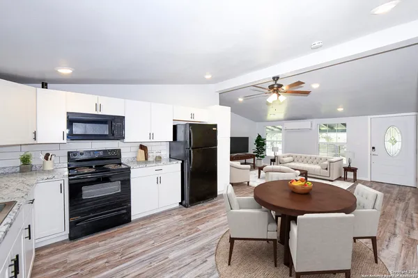 a kitchen with stainless steel appliances kitchen island granite countertop a refrigerator a stove a sink a dining table and chairs with wooden floor
