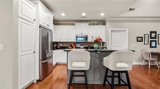 a kitchen with stainless steel appliances a refrigerator a stove top oven a sink dishwasher and white cabinets with wooden floor