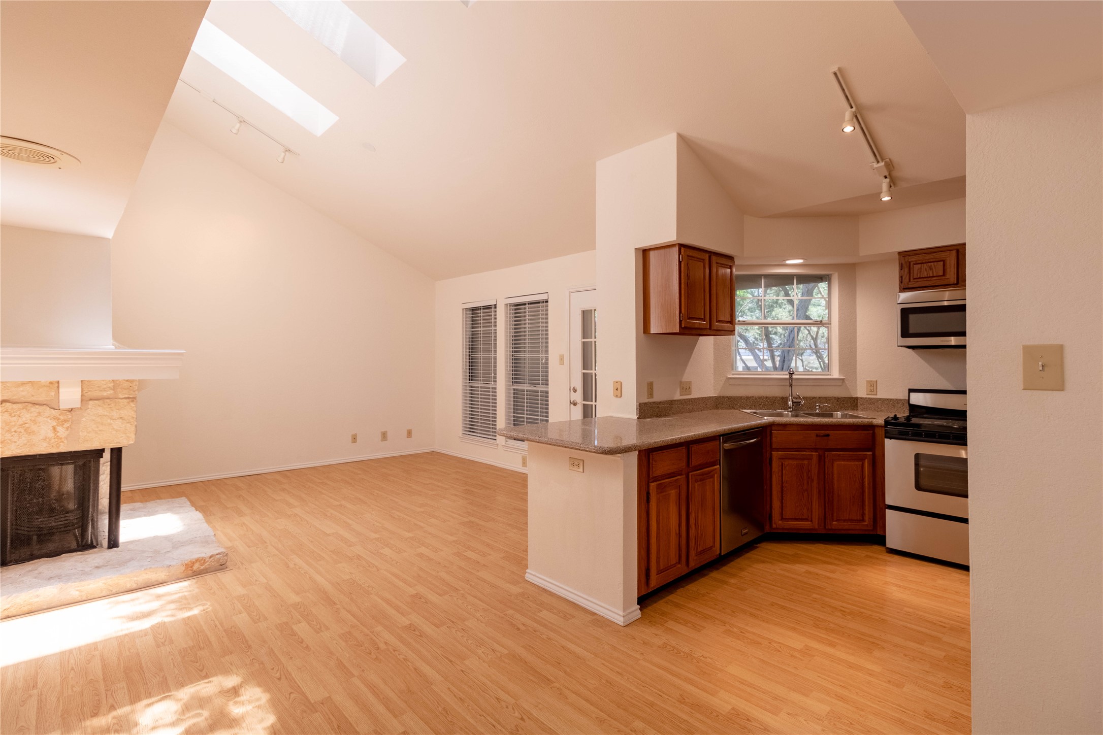 3809 Spicewood Springs Road, Unit 253 Austin, TX 78759 - Photo 8 of 23 Kitchen with wood finish cabinets, track lighting, stainless steel appliances, a skylight, and a multi sided fireplace