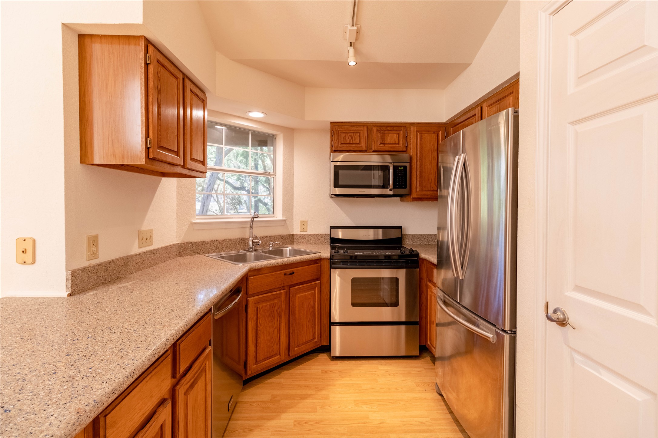 3809 Spicewood Springs Road, Unit 253 Austin, TX 78759 - Photo 9 of 23 Kitchen featuring stainless steel appliances, wood finish cabinetry, light wood-style floors, light stone counters, and rail lighting