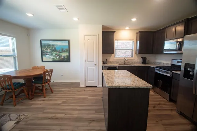 a kitchen with stainless steel appliances granite countertop a table chairs sink and cabinets