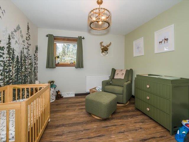 5508 Nordling Road Duluth, MN 55804 - Photo 25 of 58 Bedroom with a crib, radiator, dark wood finished floors, and a chandelier