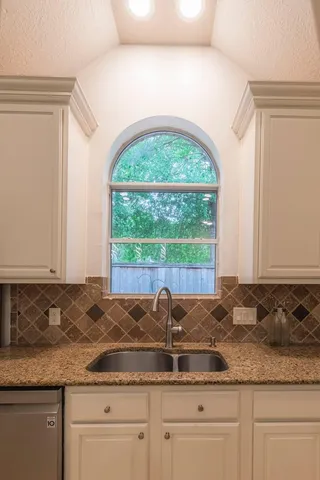 a kitchen with granite countertop a sink and white cabinets with a large window