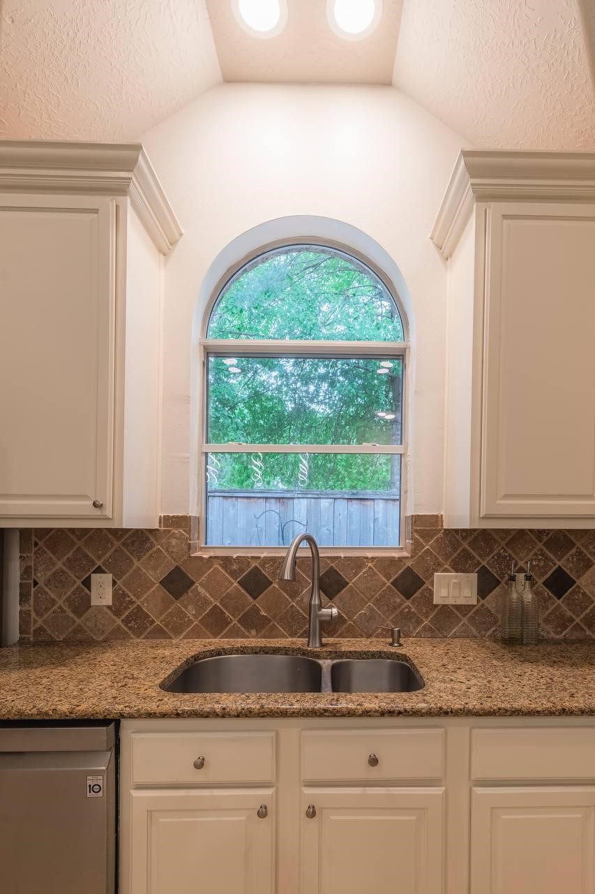6 Avenswood Place Spring, TX 77382 - Photo 11 of 22 a kitchen with granite countertop a sink and white cabinets with a large window
