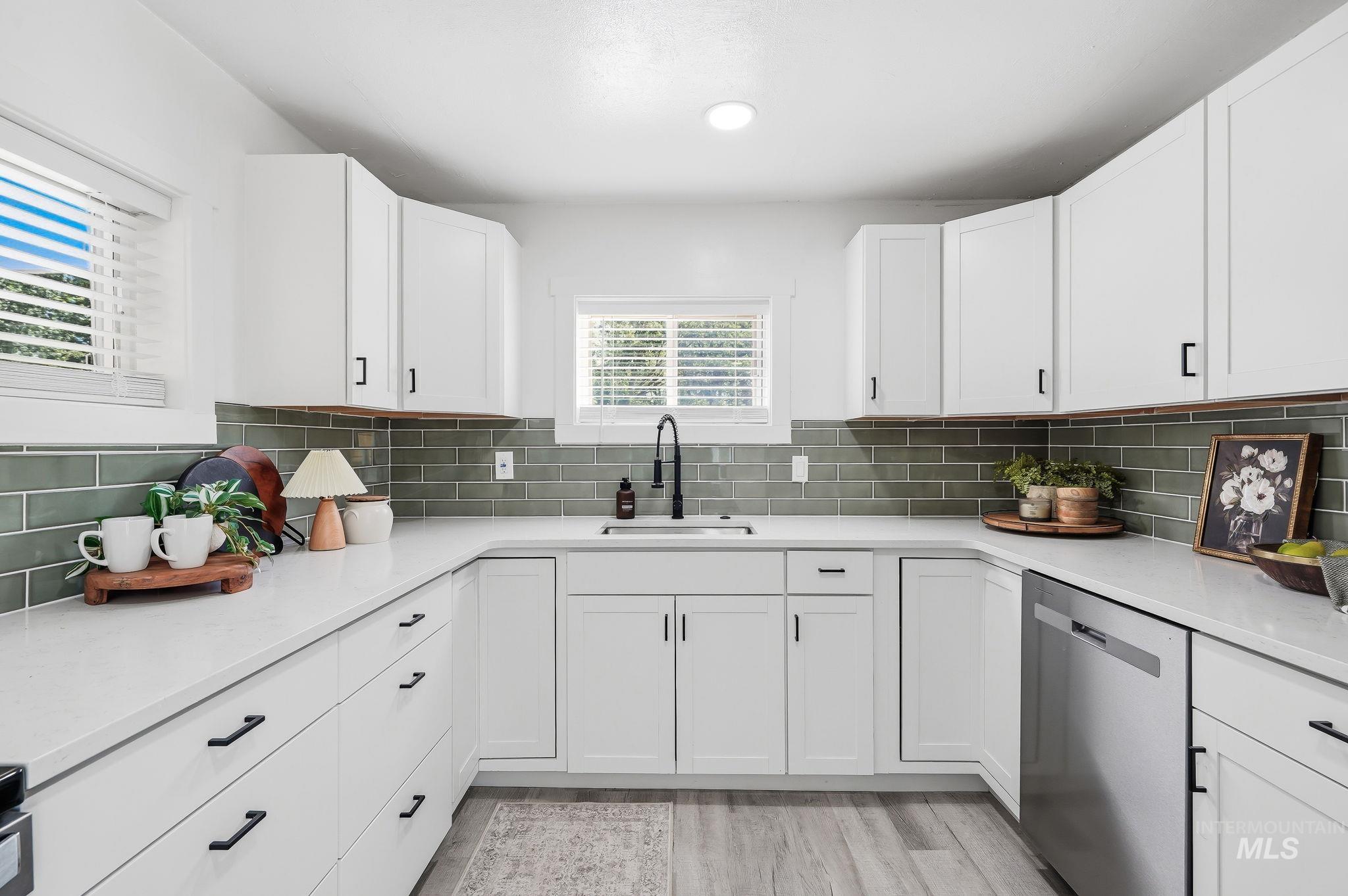2152 Artesian Road Eagle, ID 83616 - Photo 18 of 50 U-shaped kitchen featuring white cabinetry with black hardware, light-toned countertops, a green subway tile backsplash, and wood-finish flooring