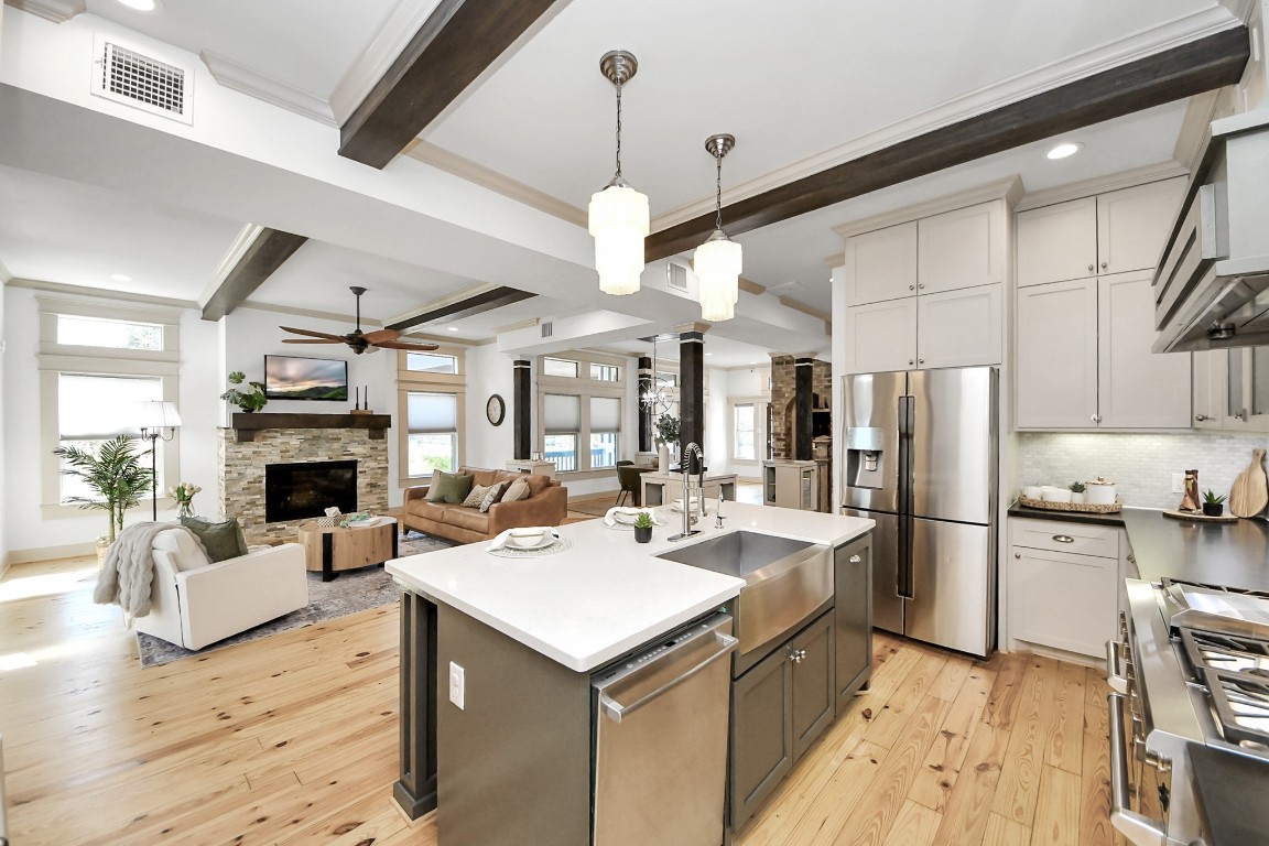 1202 Archer Street Houston, TX 77009 - Photo 19 of 47 Chefs open-concept kitchen and living area with a sleek kitchen with white cabinetry, stainless steel appliances, and a large island with abundant seating. The living room has a cozy fireplace, ceiling fan, and ample natural light, creating a warm, inviting space perfect for entertaining.