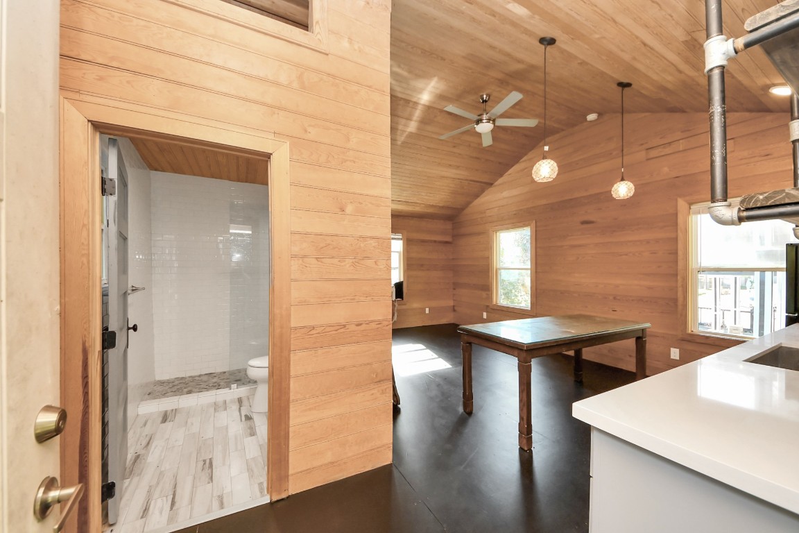 1202 Archer Street Houston, TX 77009 - Photo 42 of 47 This cozy, wood-paneled interior features an open living area with vaulted ceilings and abundant natural light, complemented by modern lighting fixtures. A visible bathroom with tiled flooring adds convenience, enhancing the space’s functional and inviting layout.