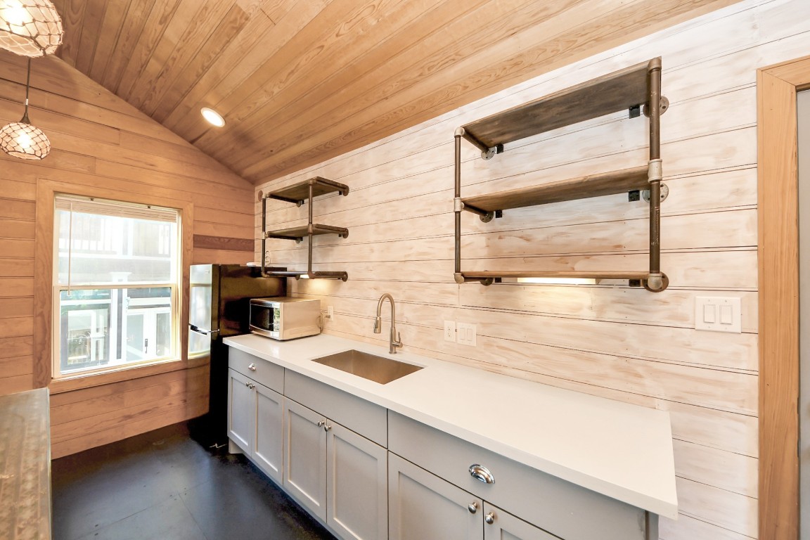 1202 Archer Street Houston, TX 77009 - Photo 45 of 47 This cozy kitchen features a vaulted wooden ceiling, modern open shelving, and a sleek countertop. A window fills the space with natural light, while a compact fridge completes the functional layout, creating a charming and rustic atmosphere.