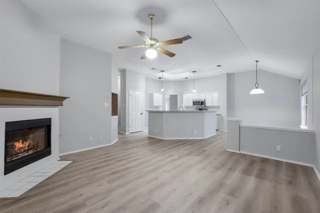 a view of a kitchen a ceiling fan a fireplace and wooden floor