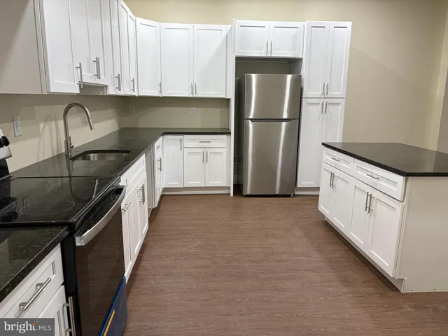 a kitchen with granite countertop a refrigerator a sink and white cabinets