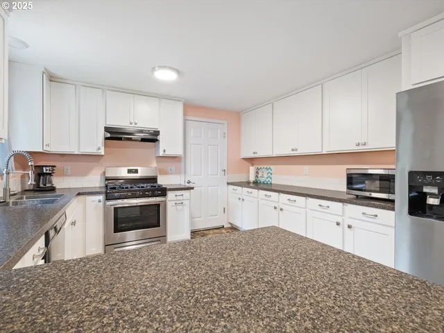 a kitchen with stainless steel appliances granite countertop a stove top oven a sink a refrigerator and white cabinets