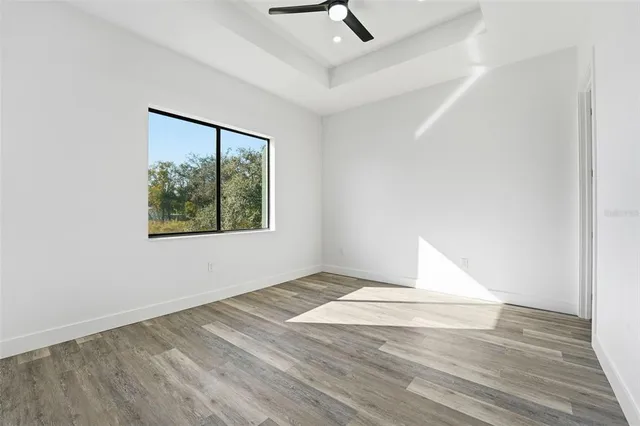 an empty room with wooden floor and way to kitchen