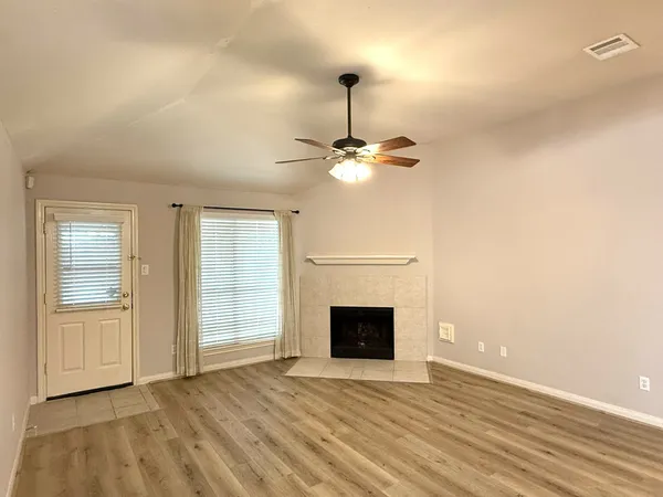 an empty room with wooden floor fireplace and windows