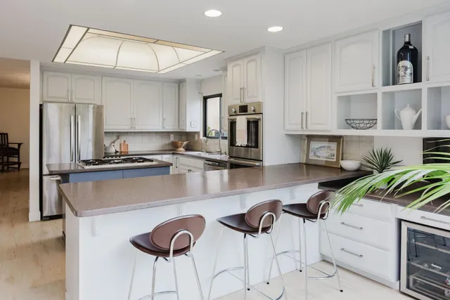 a kitchen with stainless steel appliances granite countertop a sink a stove a refrigerator cabinets and a dining table