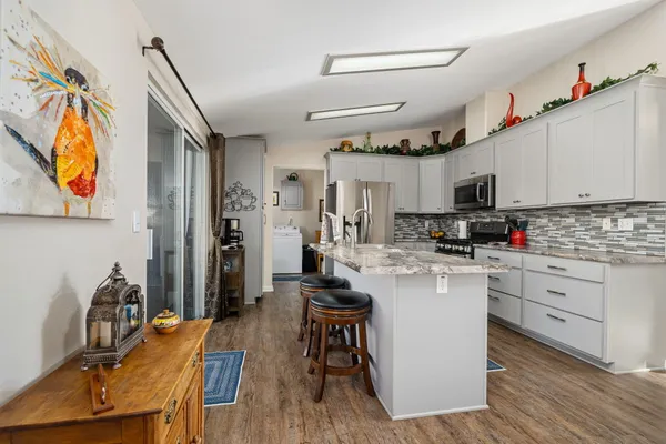 a kitchen with stainless steel appliances kitchen island granite countertop a refrigerator a stove a sink dishwasher and white cabinets with wooden floor