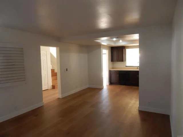 an empty room with wooden floor and kitchen view