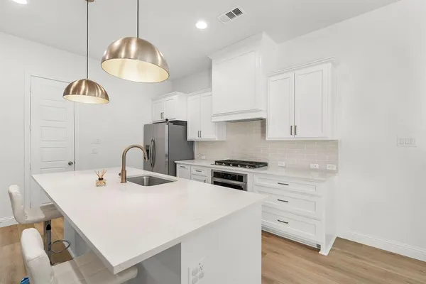 a kitchen with stainless steel appliances a sink a stove a refrigerator and white cabinets with wooden floor