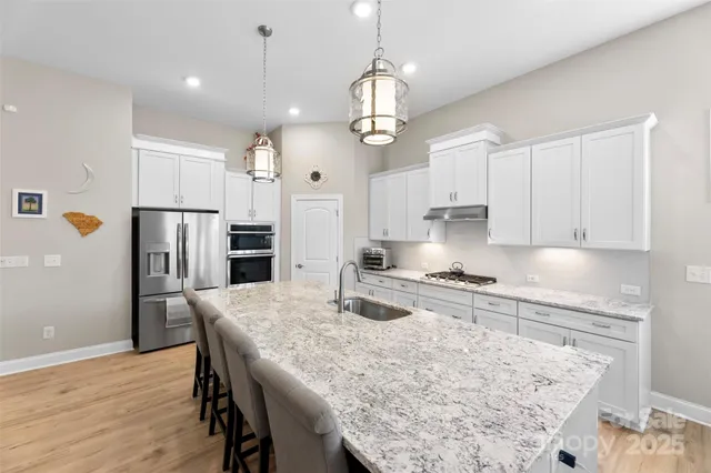 a kitchen with stainless steel appliances granite countertop a sink refrigerator a stove a dining table and chairs with wooden floor