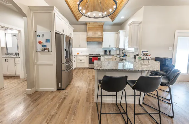 a kitchen with stainless steel appliances granite countertop a refrigerator a sink dishwasher a stove and a dining table with wooden floor