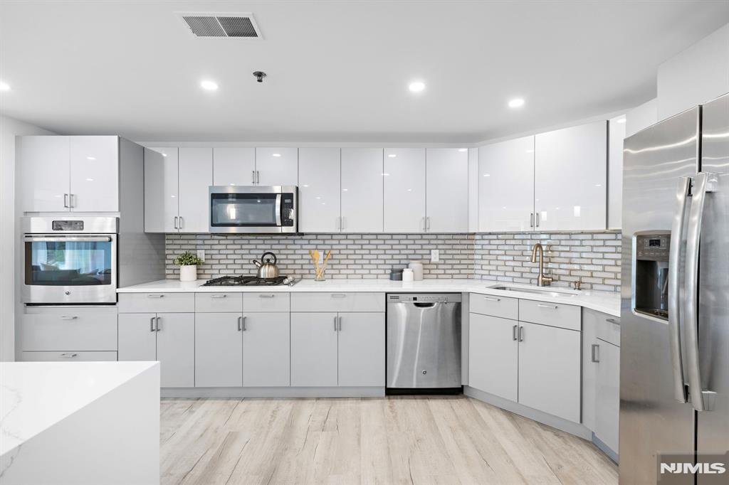 302 Smith Court Edgewater, NJ 07020 - Photo 10 of 34 a kitchen with stainless steel appliances granite countertop a stove top oven a sink dishwasher and a refrigerator with wooden floor