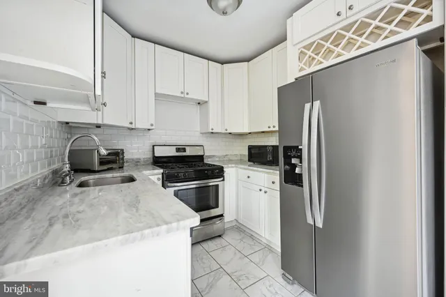 a kitchen with stainless steel appliances granite countertop a refrigerator a sink and white cabinets