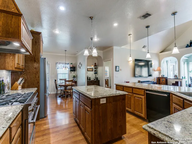 a kitchen with stainless steel appliances granite countertop a stove top oven a sink dishwasher and a dining table with wooden floor
