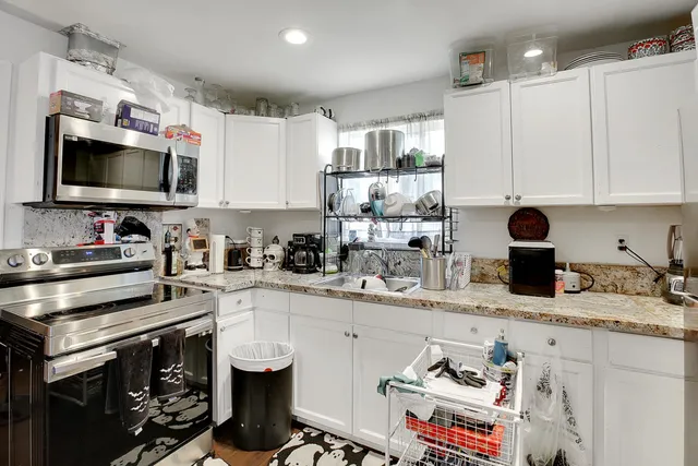 a kitchen with stainless steel appliances granite countertop a stove top oven a sink dishwasher and white cabinets with wooden floor