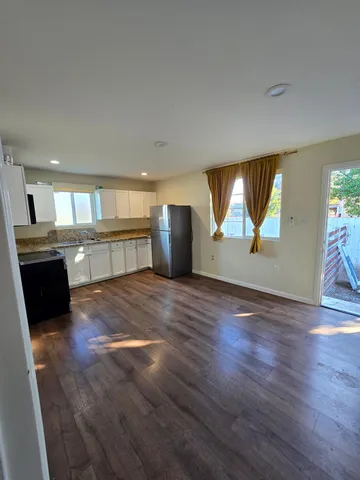 an empty room with wooden floor kitchen view and a window