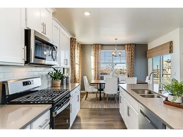 a kitchen with stainless steel appliances granite countertop a stove a sink dishwasher and white cabinets with wooden floor