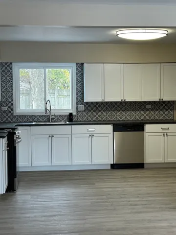 a white kitchen with granite countertop white cabinets and a wooden floor