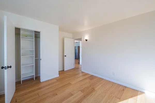 a view of an empty room with wooden floor and closet