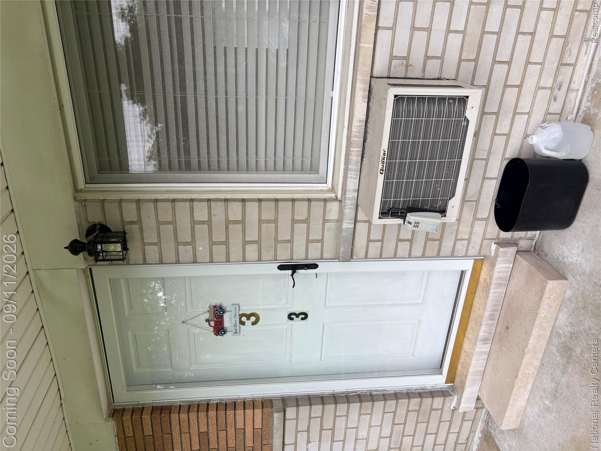 26945 Milford Road, Unit 3 New Hudson, MI 48165 - Photo 27 of 27 Brick exterior with a white entry door, exterior wall lantern, single window, and a through-wall air conditioning unit