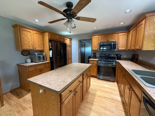 a kitchen with kitchen island granite countertop a stove top oven a sink dishwasher and wooden cabinets