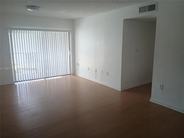 an empty room with wooden floor and windows with curtains