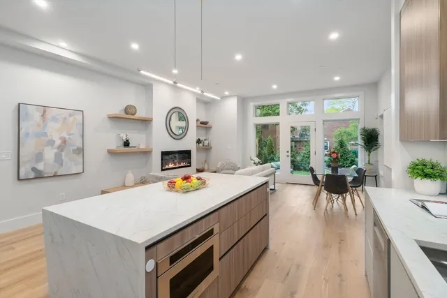 a view of a kitchen with kitchen island a large counter top space a sink stainless steel appliances cabinets and a large window