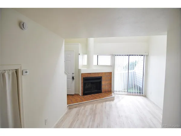 a view of an empty room with wooden floor fireplace and a window