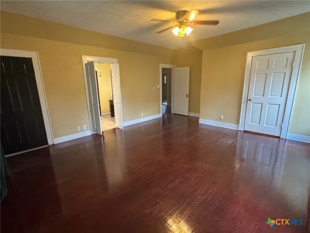 a view of an empty room with wooden floor and a ceiling fan