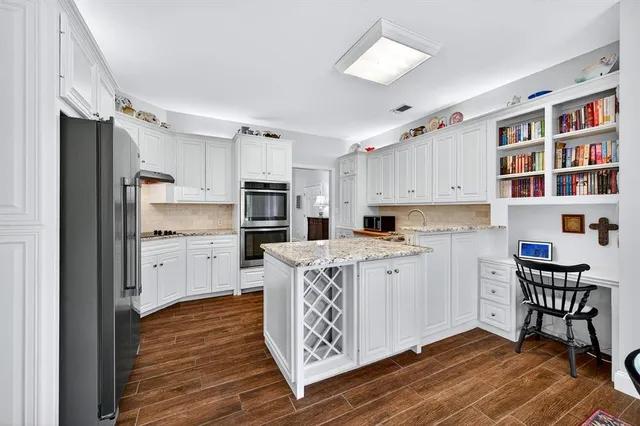 a kitchen with stainless steel appliances granite countertop a refrigerator a stove a sink dishwasher and white cabinets with wooden floor