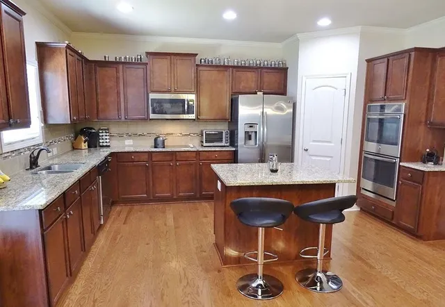 a kitchen with stainless steel appliances granite countertop a sink a stove a refrigerator cabinets and chairs