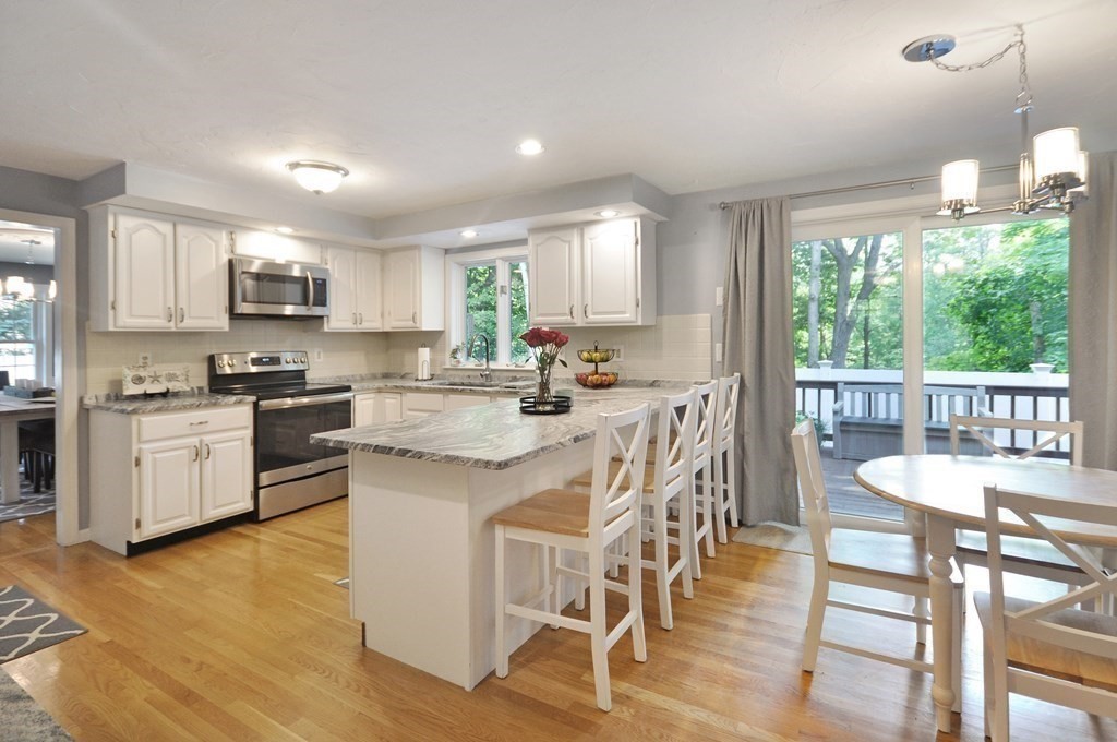 131 Sugar Road Bolton, MA 01740 - Photo 8 of 37 a kitchen with stainless steel appliances granite countertop a stove a sink a microwave a dining table and chairs with wooden floor