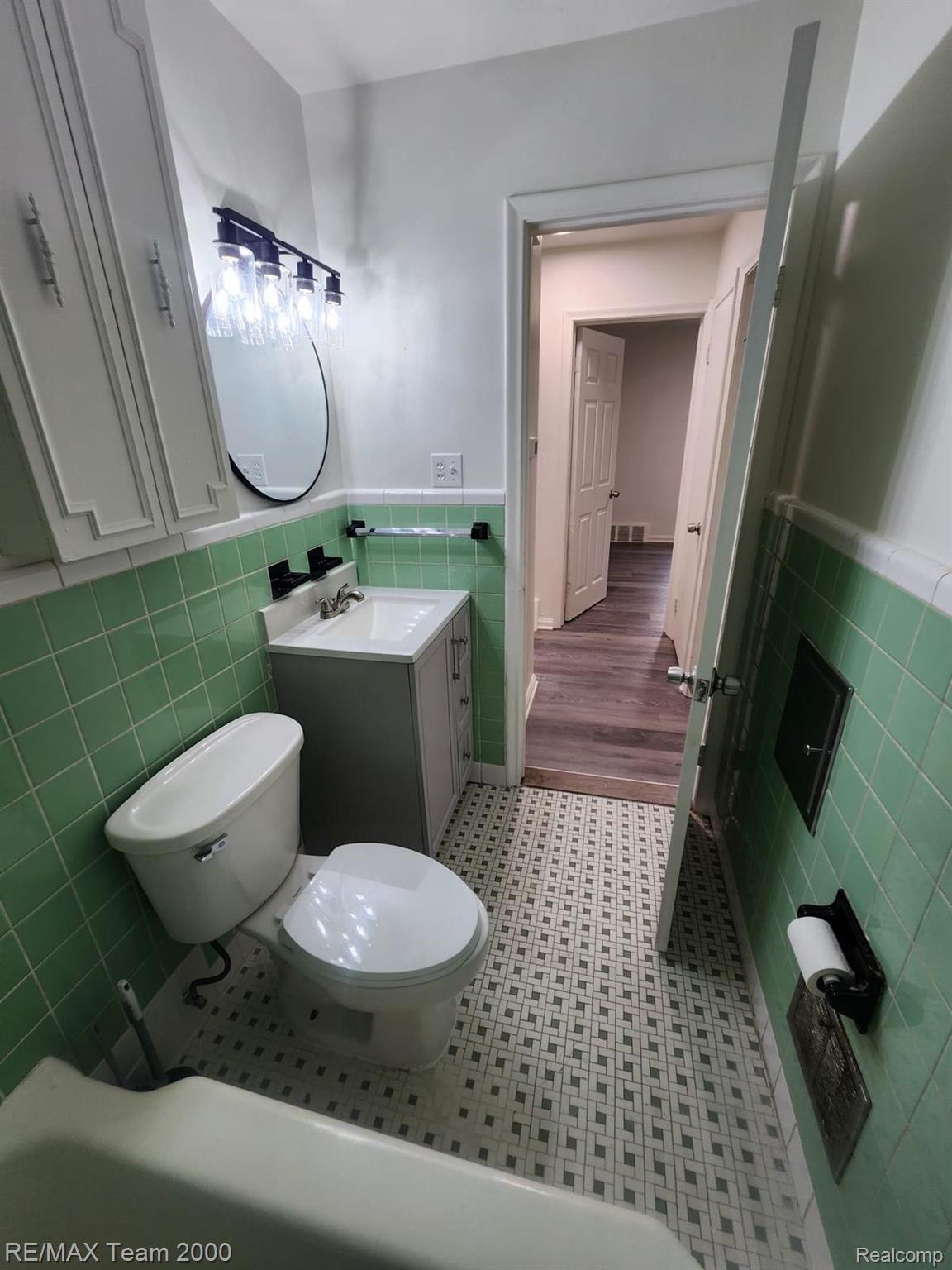 8244 Heyden Detroit, MI 48228 - Photo 13 of 21 Classic bathroom featuring vintage-inspired tile flooring in a geometric pattern, green subway tile wainscoting, white ceramic fixtures, pedestal sink with chrome hardware, and arched mirror with wall-mounted lighting