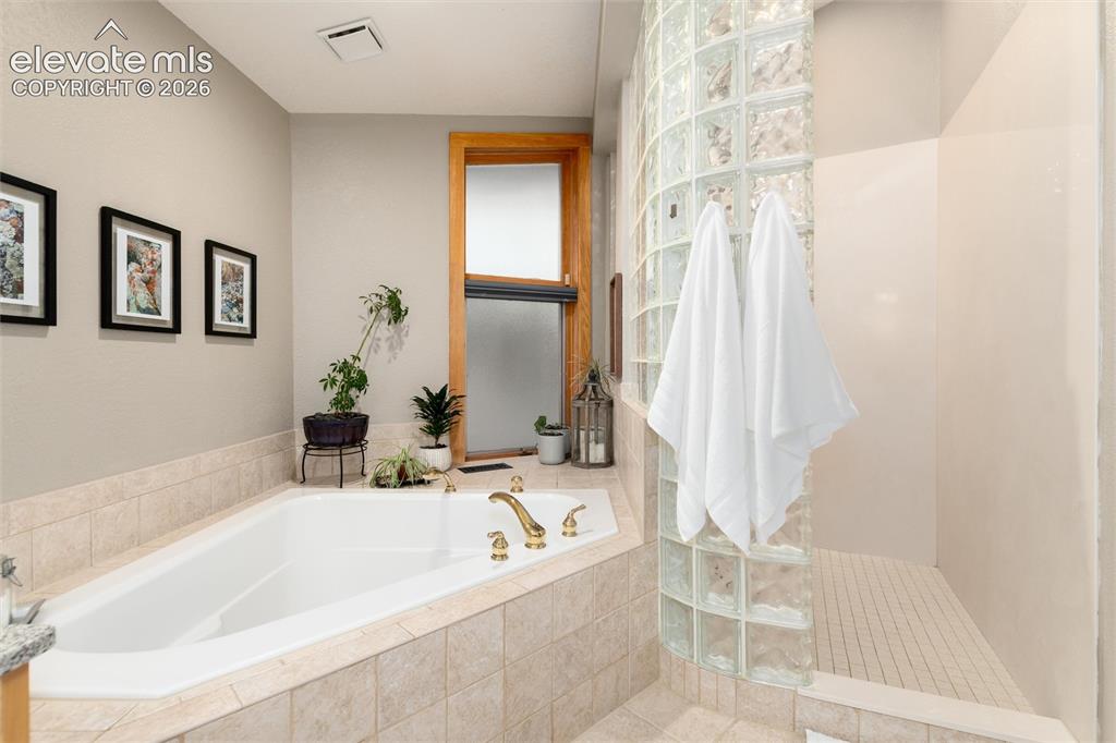 12730 Bridle Bit Road Colorado Springs, CO 80908 - Photo 28 of 50 Soaking tub with brass fixtures, surrounded by neutral-toned tiled decking