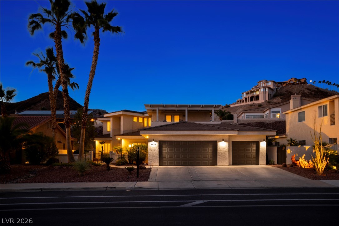 1135 Calico Ridge Drive Henderson, NV 89011 - Photo 77 of 86 An inviting desert home with illuminated facades and established landscaping against a deep twilight sky.