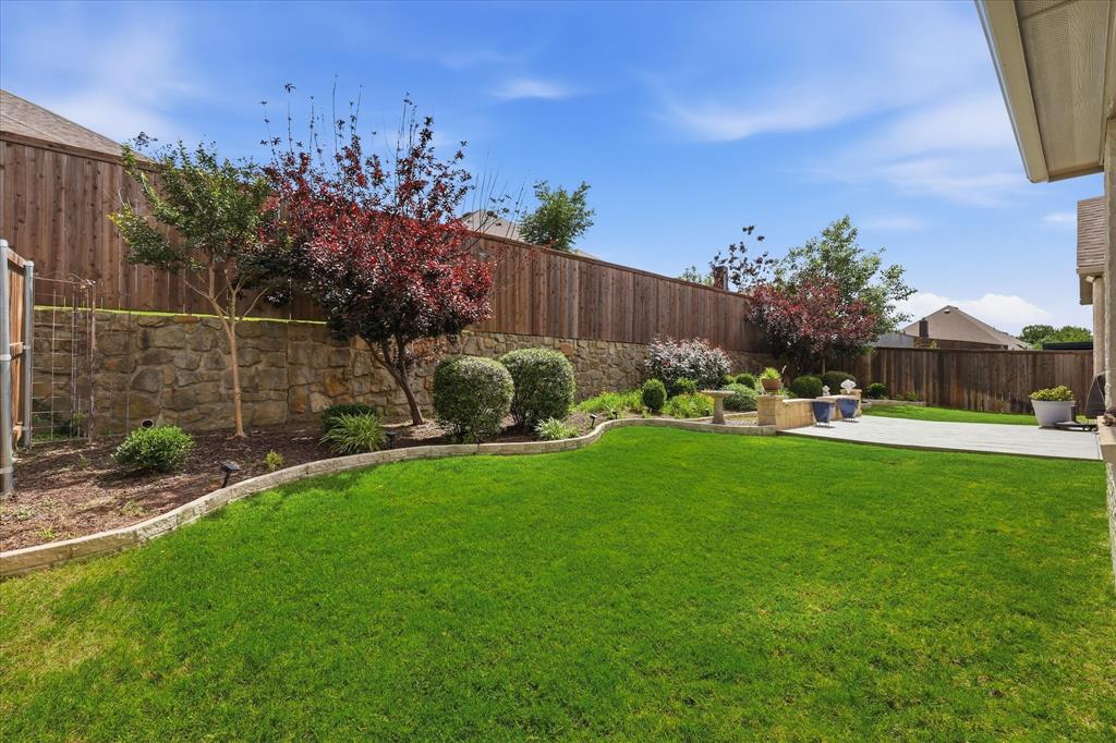 9708 Surveyor Road Oak Point, TX 75068 - Photo 33 of 34 Expansive backyard featuring a lush lawn, a stone retaining wall, and a wooden privacy fence