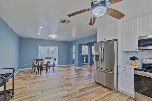 a kitchen with stainless steel appliances granite countertop a refrigerator a microwave a stove and a dining table with wooden floor