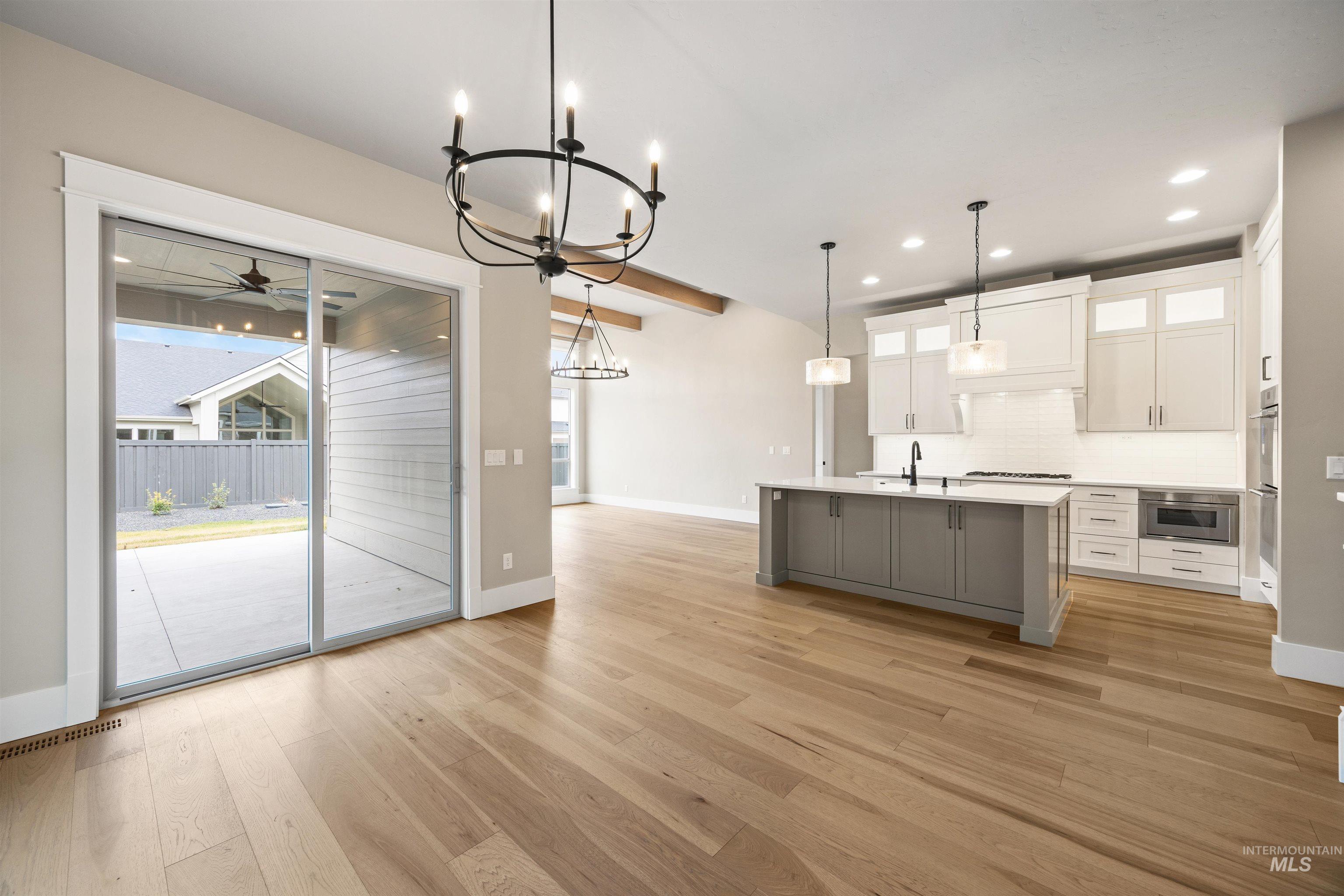 934 East Escalation Street Meridian, ID 83642 - Photo 20 of 50 Two tone kitchen featuring suspended lighting, a center island with sink, light wood-style floors, glass insert cabinets, and beamed ceiling