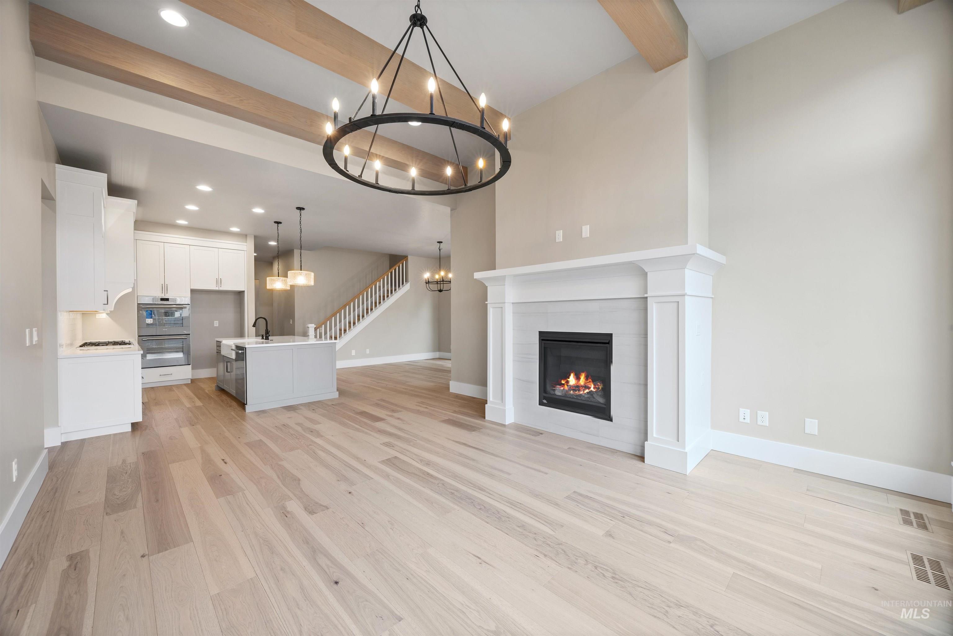 934 East Escalation Street Meridian, ID 83642 - Photo 22 of 50 Unfurnished living room featuring beam ceiling, a chandelier, light wood-style floors, and a tile fireplace