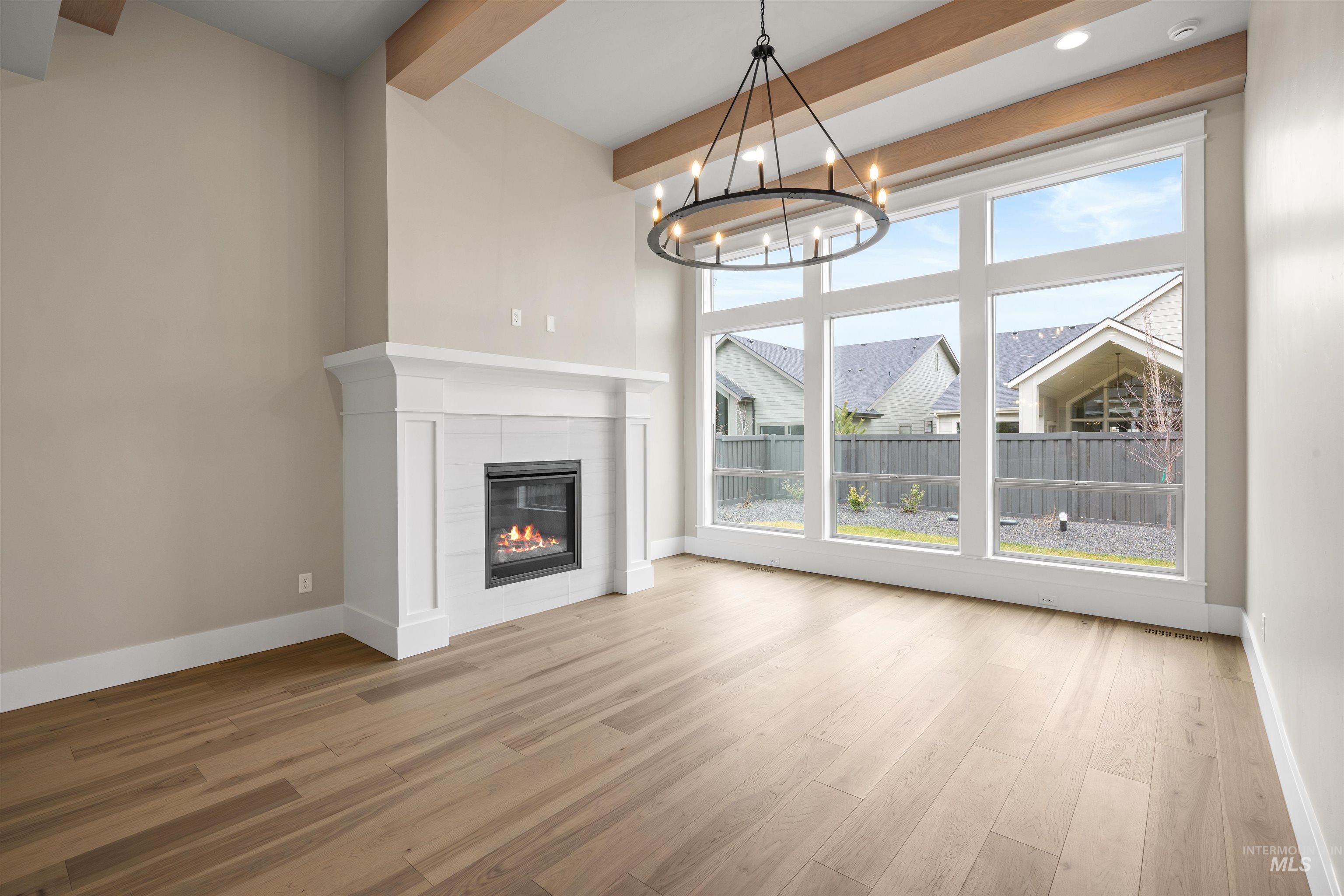 934 East Escalation Street Meridian, ID 83642 - Photo 24 of 50 Unfurnished living room featuring light wood-style flooring, a tile fireplace, beam ceiling, and a chandelier