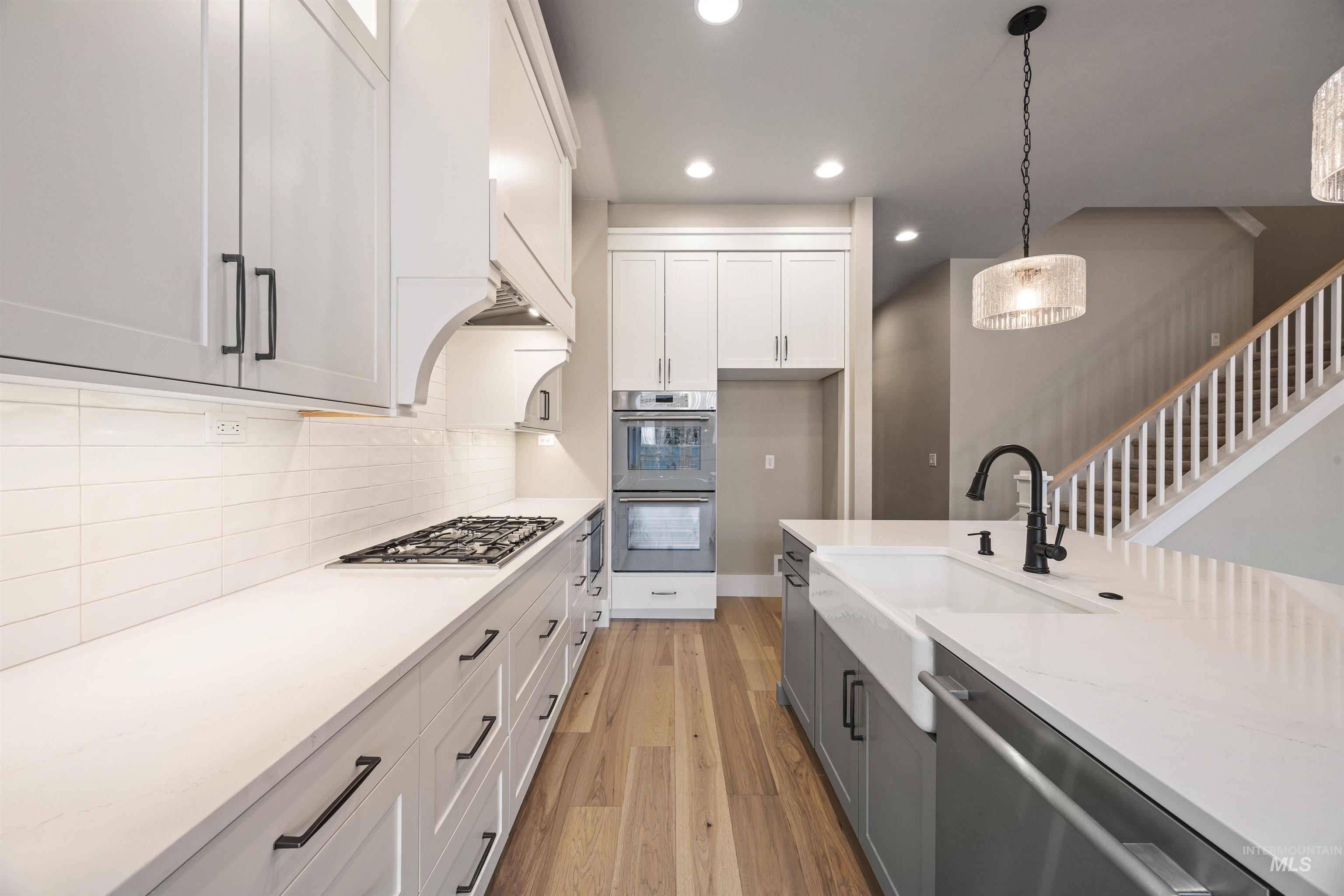934 East Escalation Street Meridian, ID 83642 - Photo 25 of 50 Kitchen featuring two tone cabinets, light wood-style floors, stainless steel appliances, light stone countertops, and decorative light fixtures