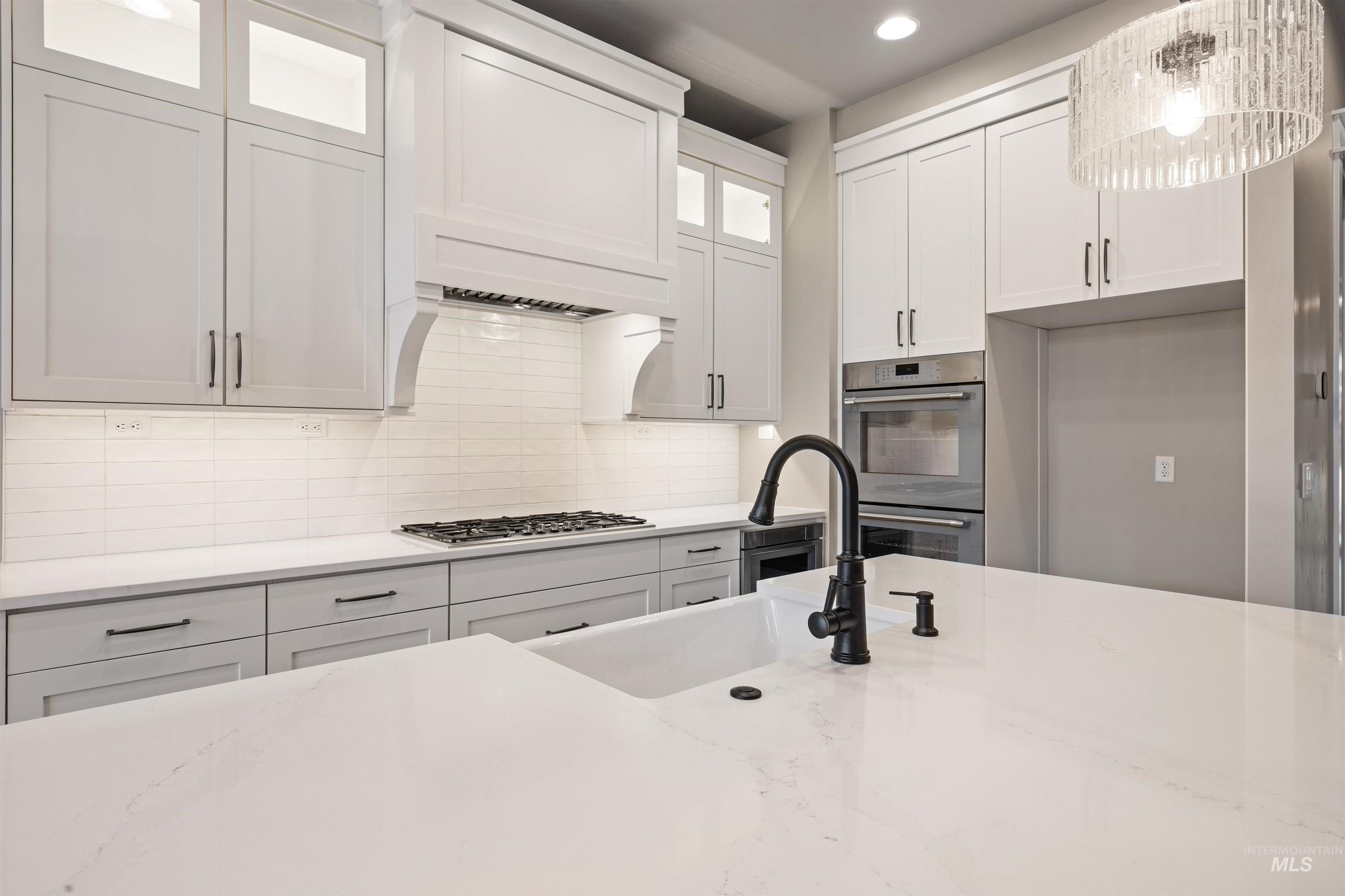 934 East Escalation Street Meridian, ID 83642 - Photo 27 of 50 Kitchen with glass fronted cabinets, tasteful backsplash, white cabinetry, stainless steel appliances, and light stone counters